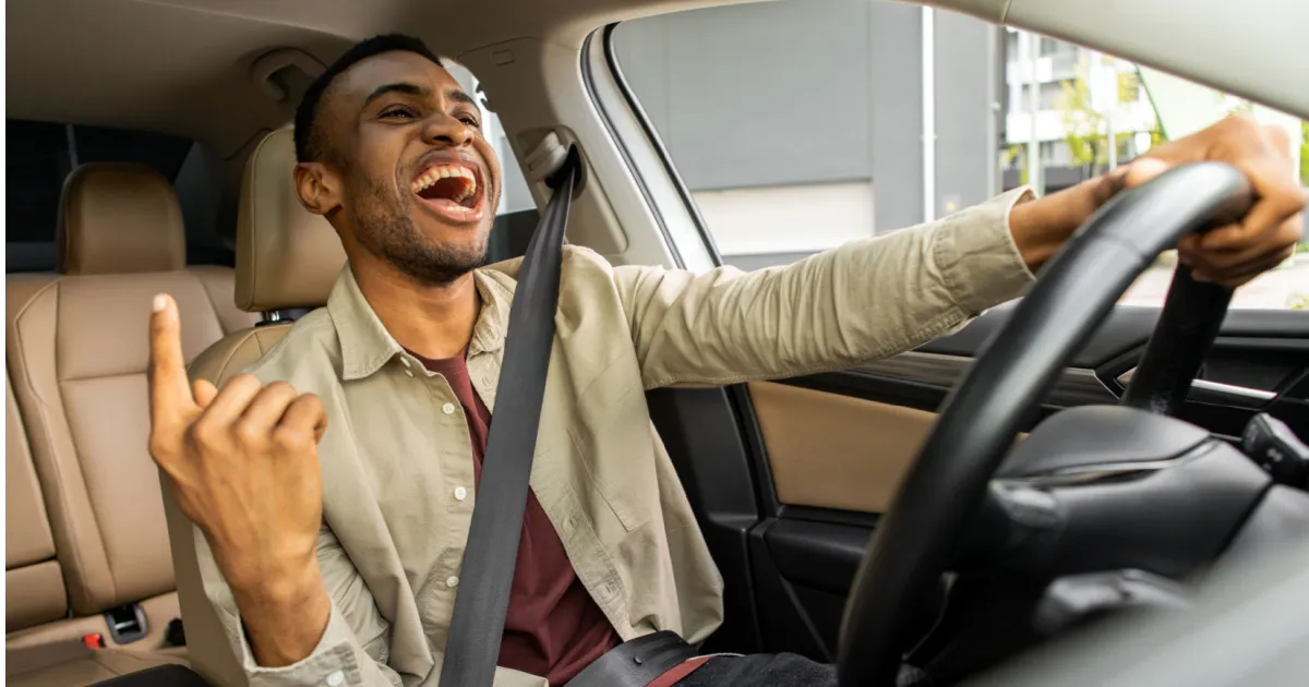 Joyful black man dancing in car, singing while driving his car