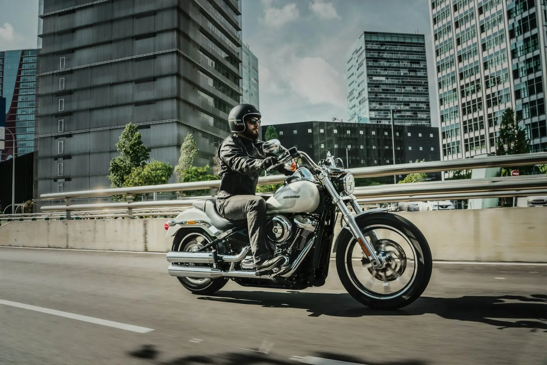 A person wearing a helmet and leather jacket riding a cruiser-style motorcycle on a city highway.