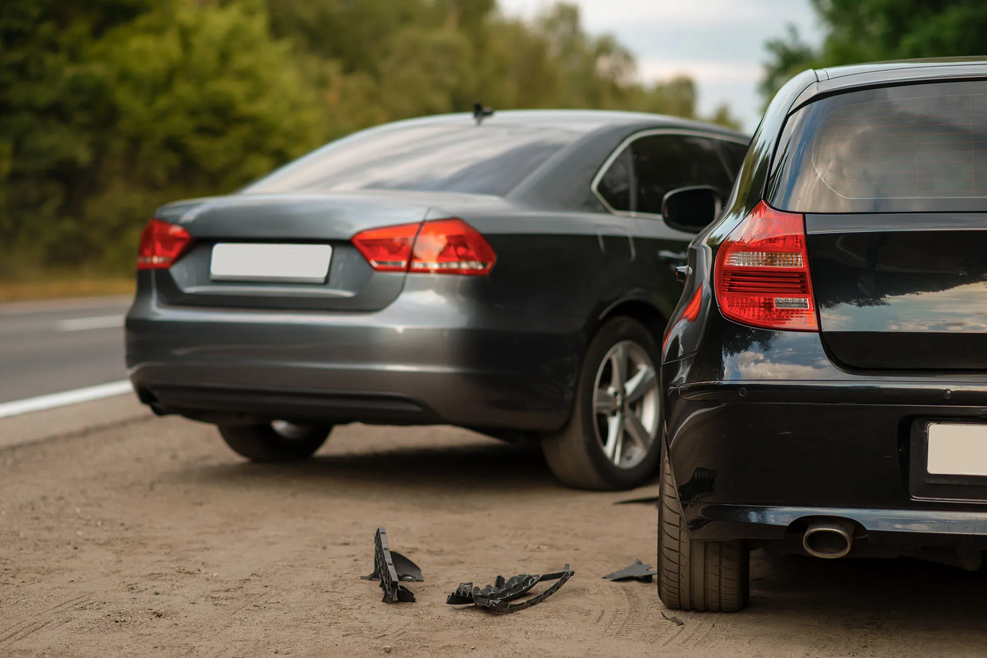 The rear view of two cars pulled over on the side of a road with debris from a collision scattered on the ground.