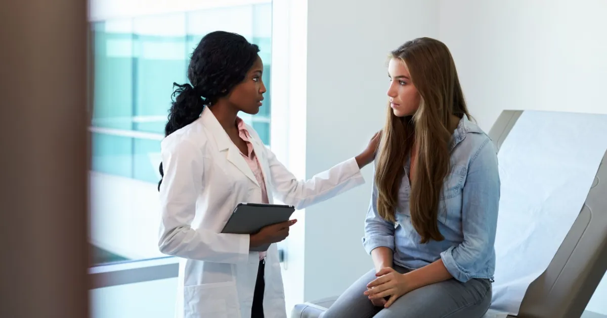 A doctor in a white coat comforting a patient sitting on an examination table.