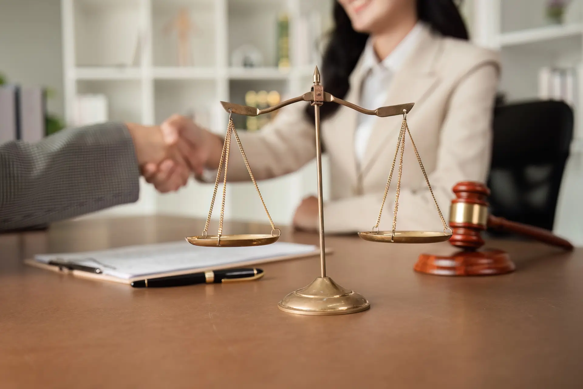 Lawyers shaking hands with scales in foreground.