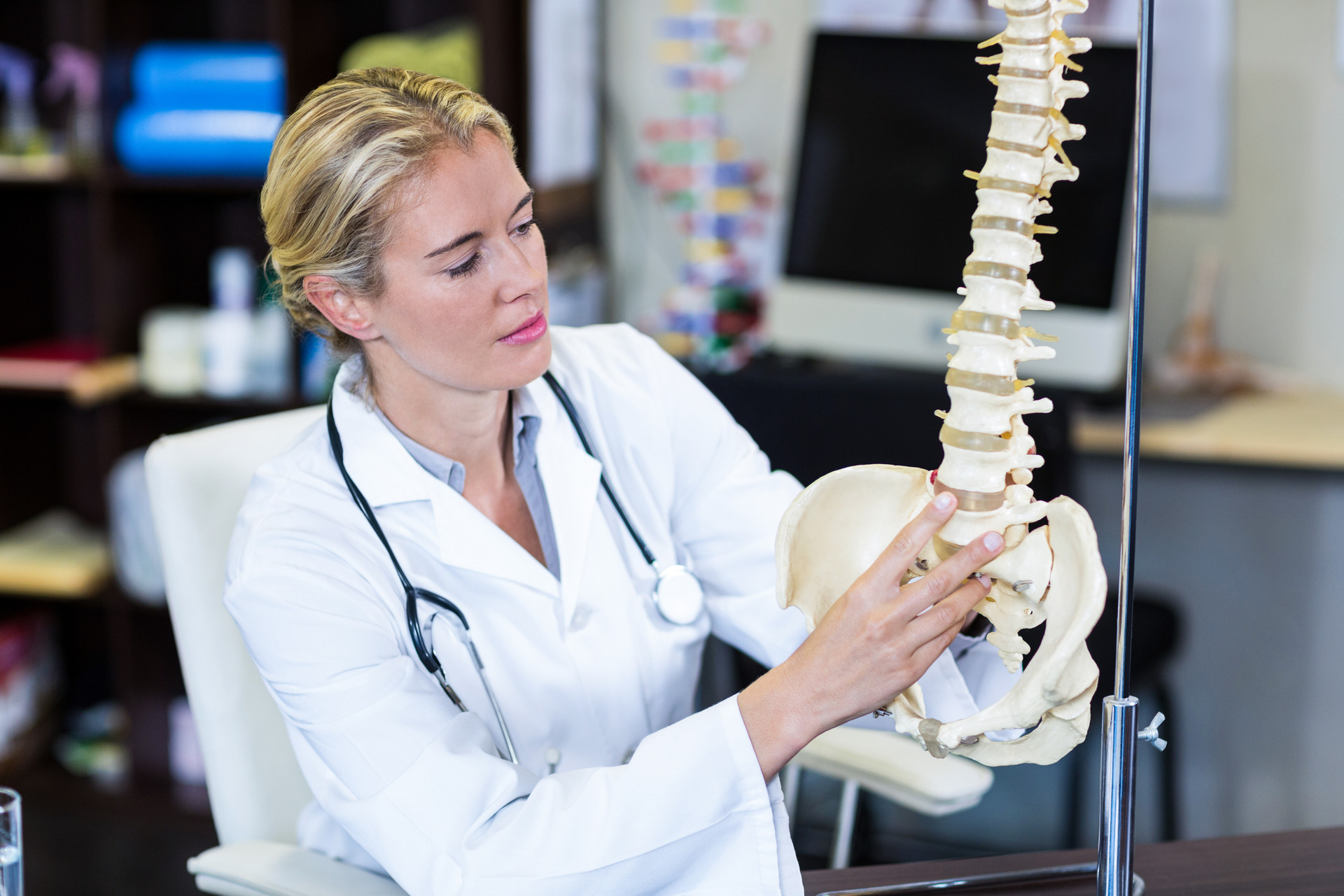 A medical professional in a lab coat pointing to a model of a human spine.