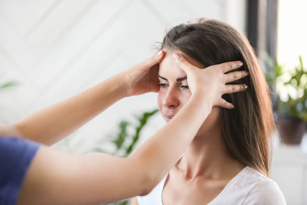A professional therapist providing a relaxing head massage to a young woman in a bright, indoor setting.