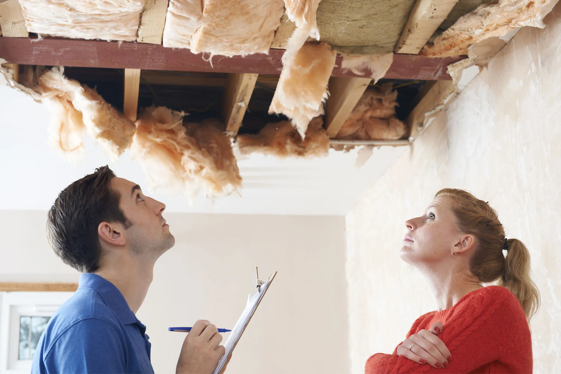A contractor with a clipboard and a homeowner looking up at damaged ceiling insulation.