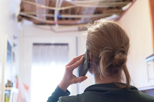 Woman on the phone looking at a damaged ceiling in her home.