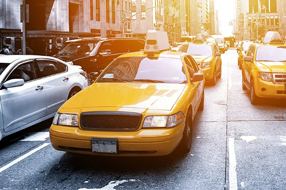 A yellow taxicab navigating through heavy traffic on a city street during the day.